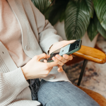 Person in gemütlicher Kleidung sitzt auf einem Sessel und tippt auf einem Smartphone – Symbol für mobiles Arbeiten oder Mobile Recruiting.