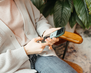 Person in gemütlicher Kleidung sitzt auf einem Sessel und tippt auf einem Smartphone – Symbol für mobiles Arbeiten oder Mobile Recruiting.